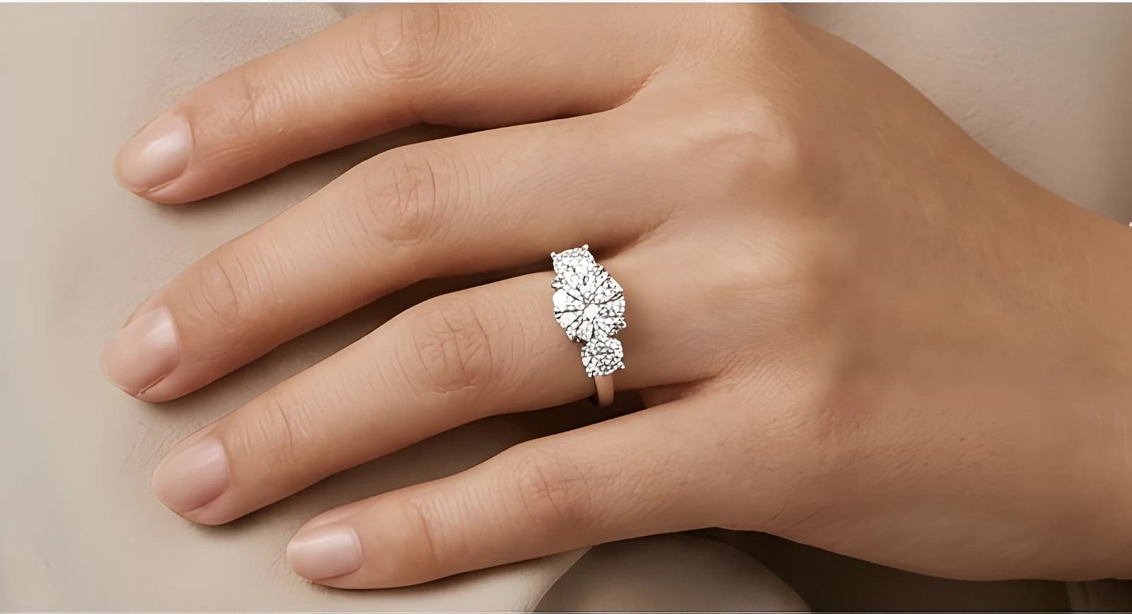 The Vesta three-stone ring in white gold on a relaxed hand against beige fabric